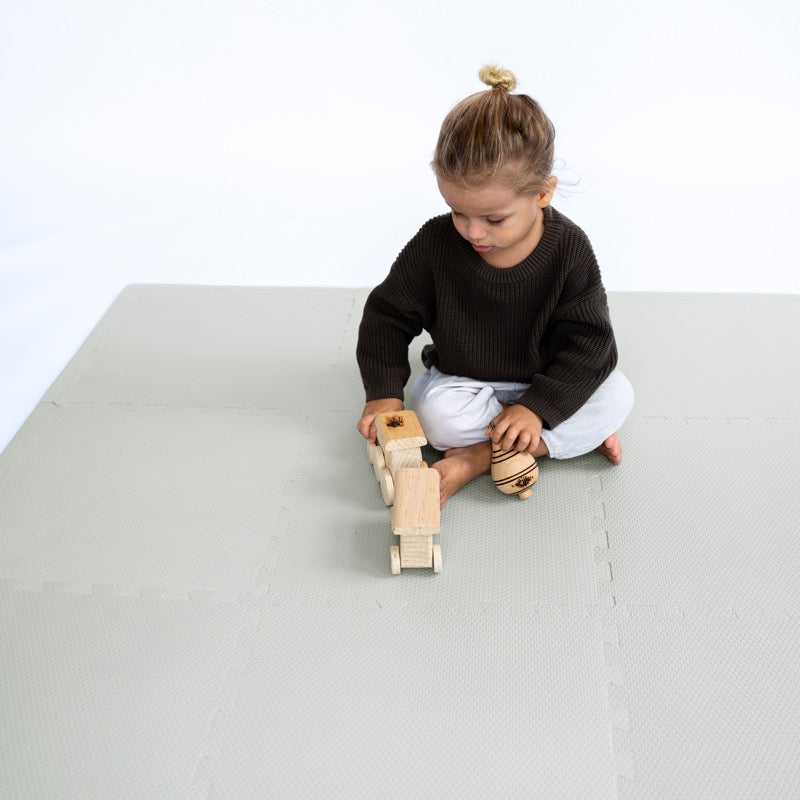 Ein Kind spielt mit einem Holzzug auf der Classic Spielmatte in &quot;Stone&quot; Grau von Toddlekind