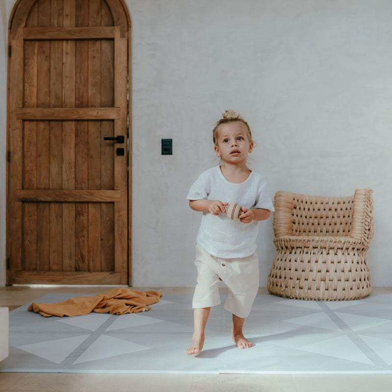 Stehendes Kind im Kinderzimmer auf der Spielmatte Kyte in &quot;Soft Storm&quot; Grau von Toddlekind mit Dreieckmuster