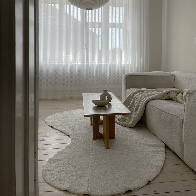 Weisser Teppich in Wolkenform von We are bitte in einem Wohnzimmer. Auf ihm steht ein Sofa und ein Couctisch. 