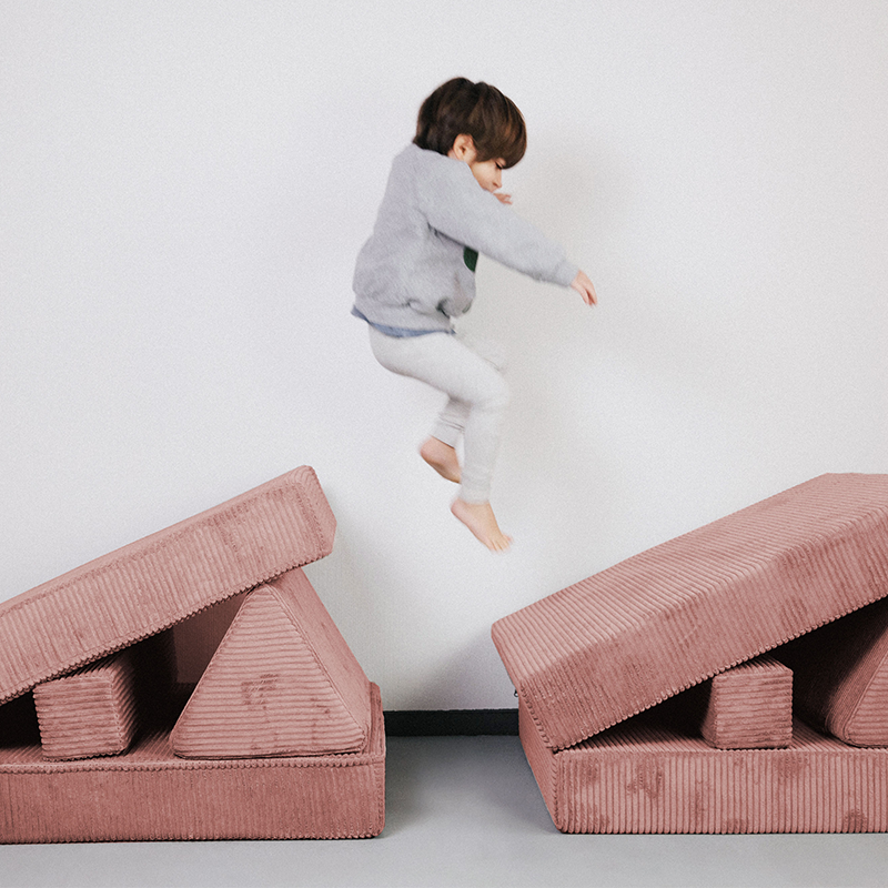 Kind spielt auf dem Spielsofa für Kinder aus weichem Cord in Pink von Wonderwuzz.