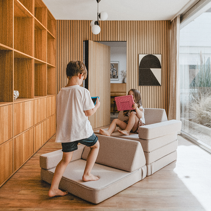 Kinder die mit dem Wonderwuzz Spielsofa mit 8 modularen Teilen 'Oh so sofy' in der Farbe Beigemarie spielen und darauf sitzen.