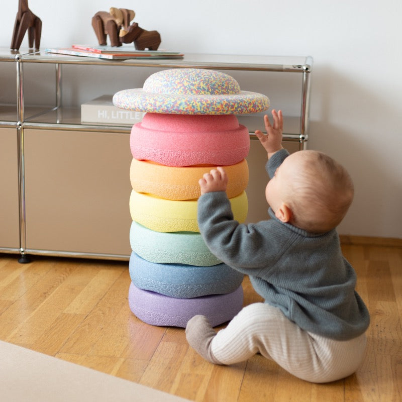 Ein kleines Kind spielt mit einem Stapel Pastell-Stapelsteine + Confetti Board